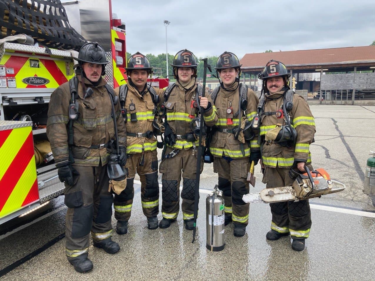 Five members in turnout gear and air packs at burn training